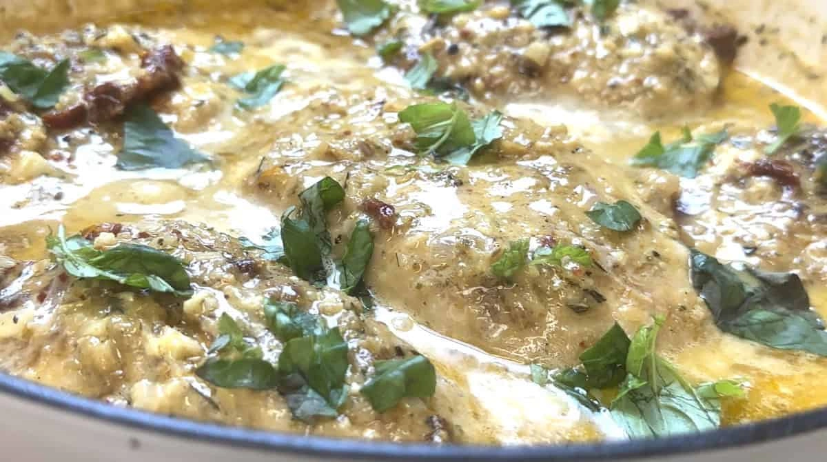 Creamy chicken thighs with herbs and spices in a savory sauce, garnished with fresh parsley leaves.